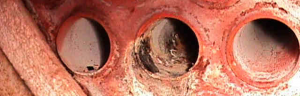 Photograph of corroded or scaled boiler tubes or pipes, showing internal damage and deposits.