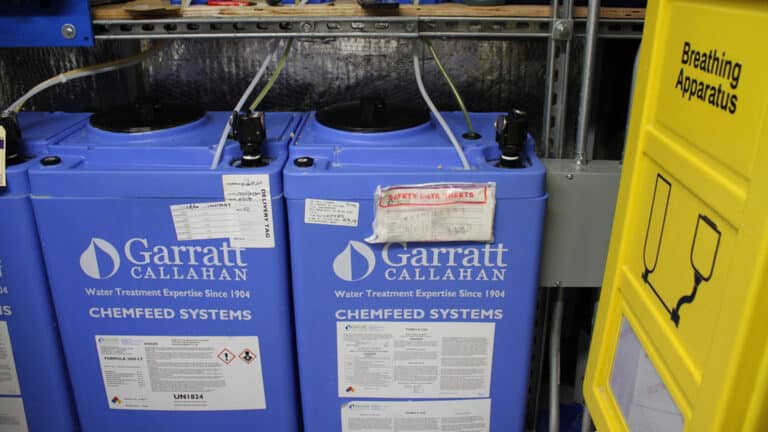 Blue Garratt Callahan Chemfeed Systems water treatment tanks with tubing next to a yellow breathing apparatus cabinet.