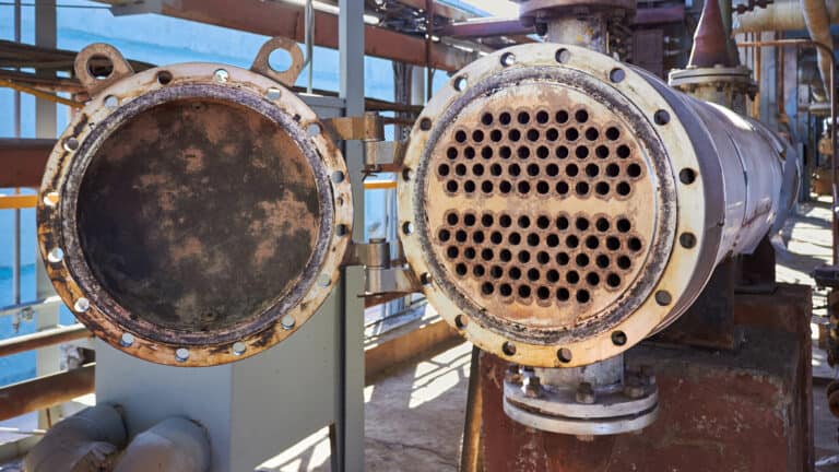 An open industrial shell-and-tube heat exchanger showing the internal tube sheet and piping inside a manufacturing facility.