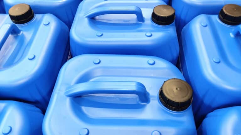 Close-up view of blue plastic chemical containers with black screw caps and molded handles.