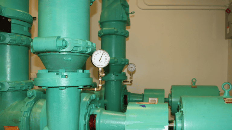 Teal industrial pipes and machinery with circular pressure gauges in a utility room.