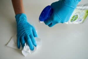 A person wearing blue gloves and cleaning a surface with a spray bottle and a paper towel