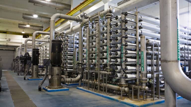 Industrial reverse osmosis water treatment plant with rows of stacked white membrane vessels, pumps, and stainless steel piping.