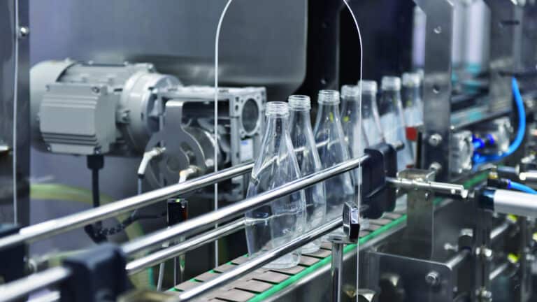 Clear glass bottles moving along an automated conveyor belt line inside a beverage manufacturing plant.