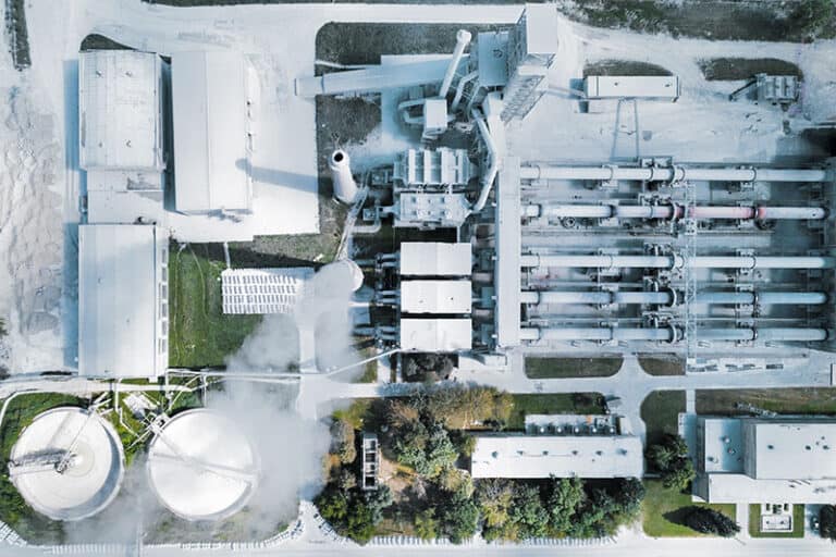 Aerial view of a large cement manufacturing plant with multiple structures, silos, and rotary kilns.