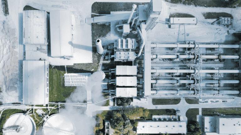 Aerial view of a large cement manufacturing plant with multiple structures, silos, and rotary kilns.