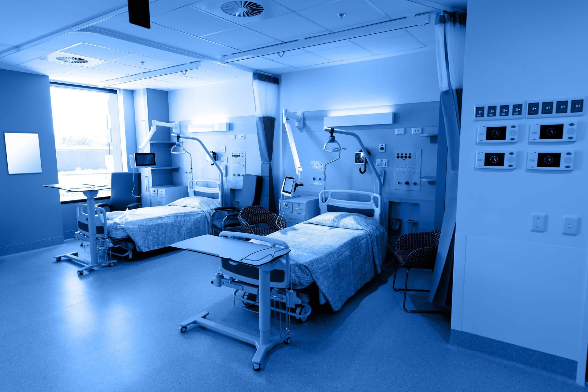 A clean empty hospital rooom with two beds a stylized blue and sepia tone.