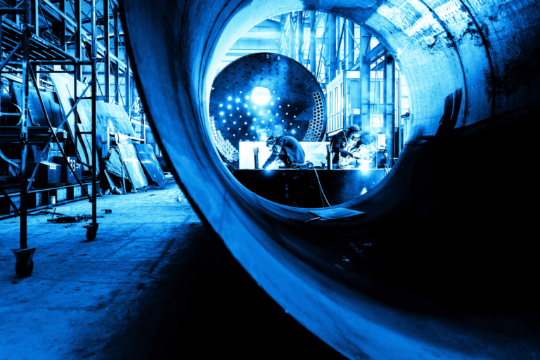 A welder creating sparks in a warhouse viewed through huge pipes, stylized with a blue and sepia tone.